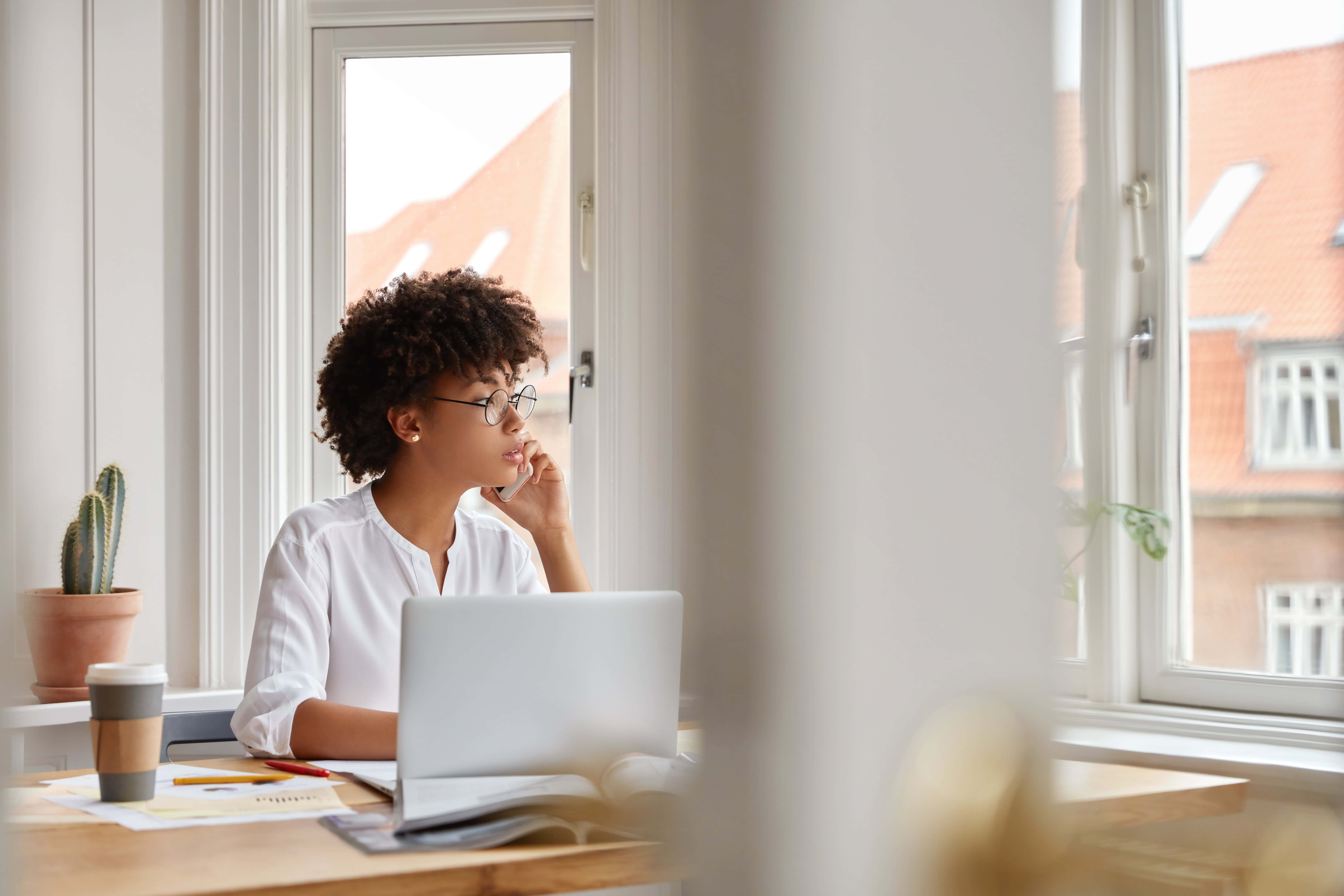 Office worker working at a desk with a laptop by the window.
