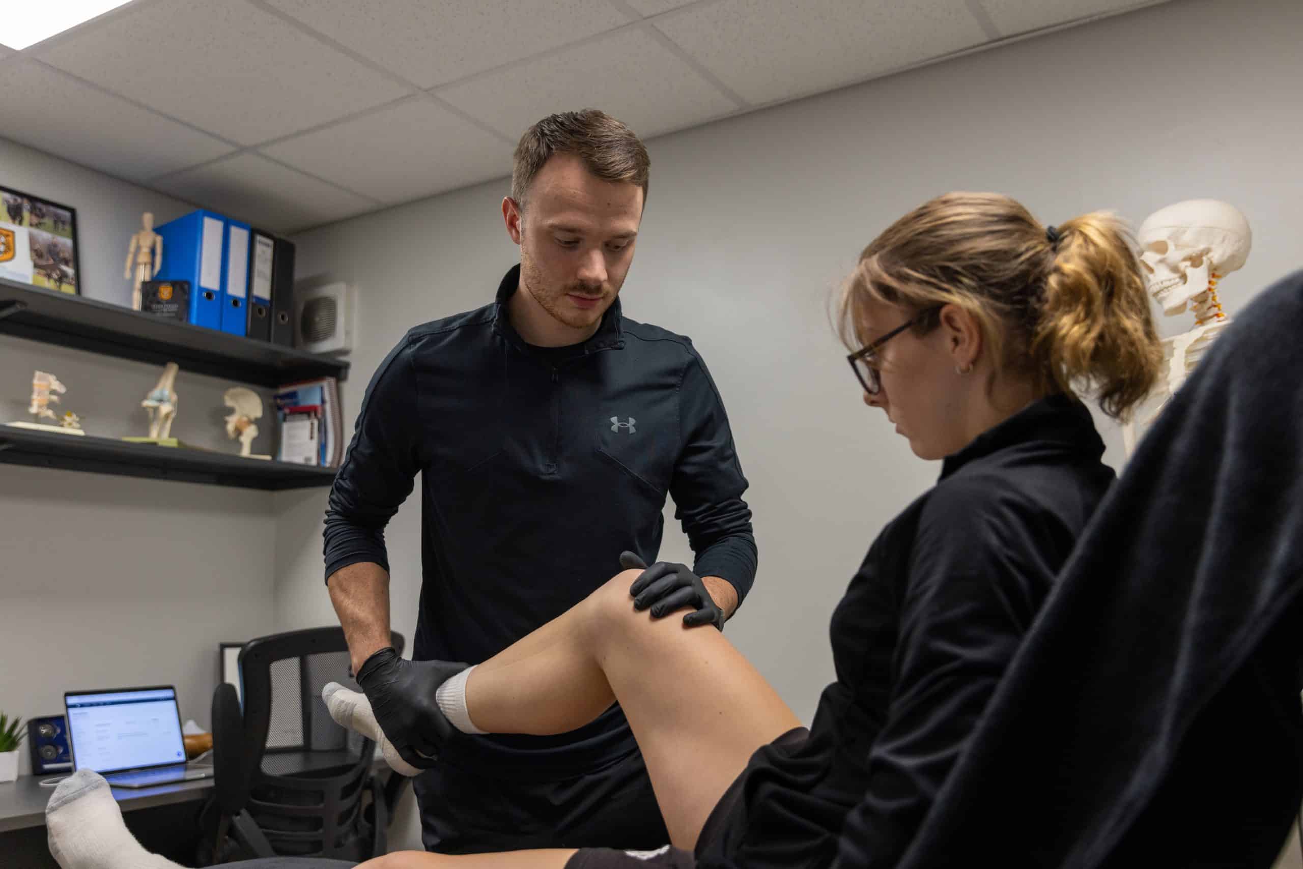 Medical professional examining patient's knee in clinic setting.