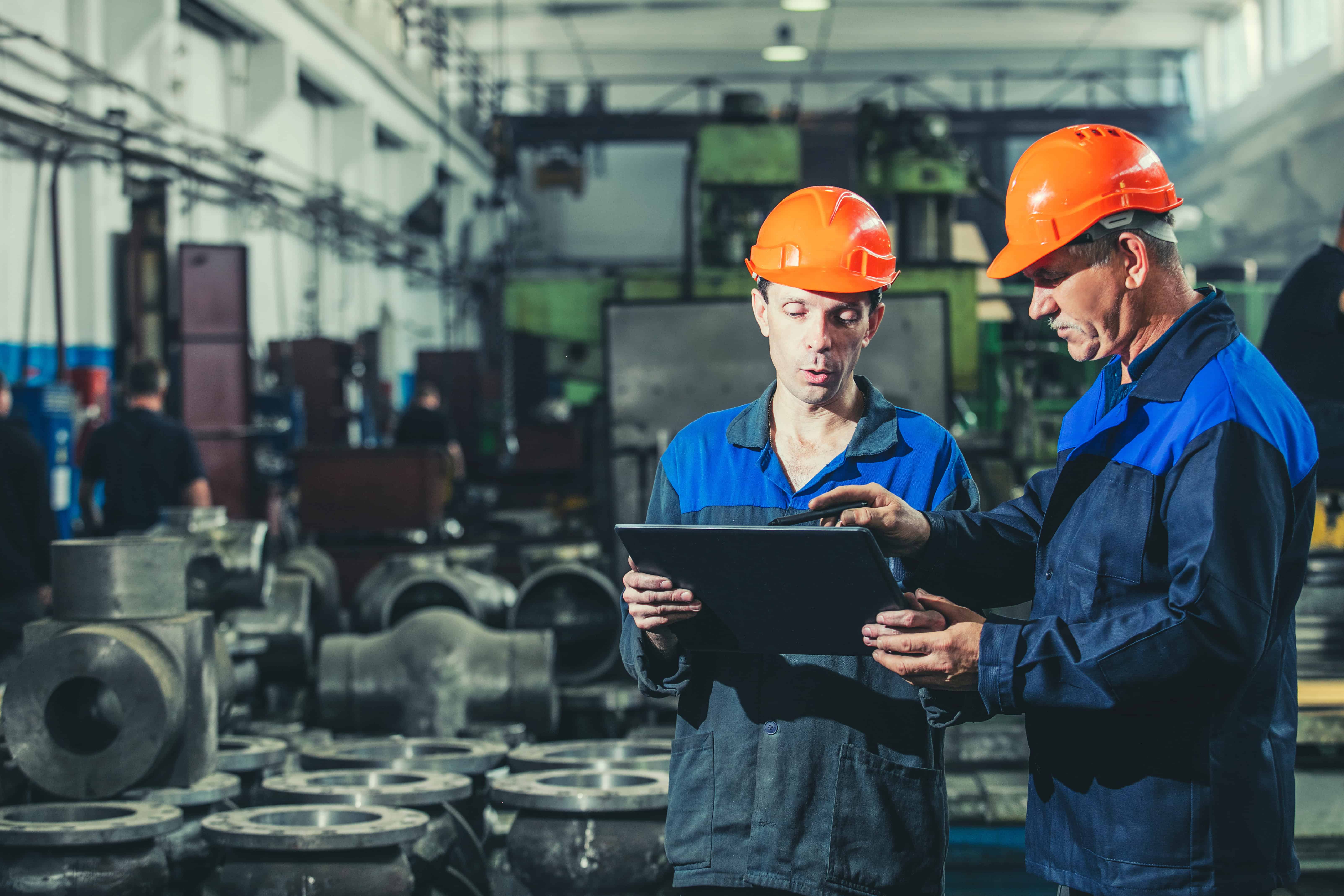 Manufacturing workers in safety gear inspecting equipment in factory.