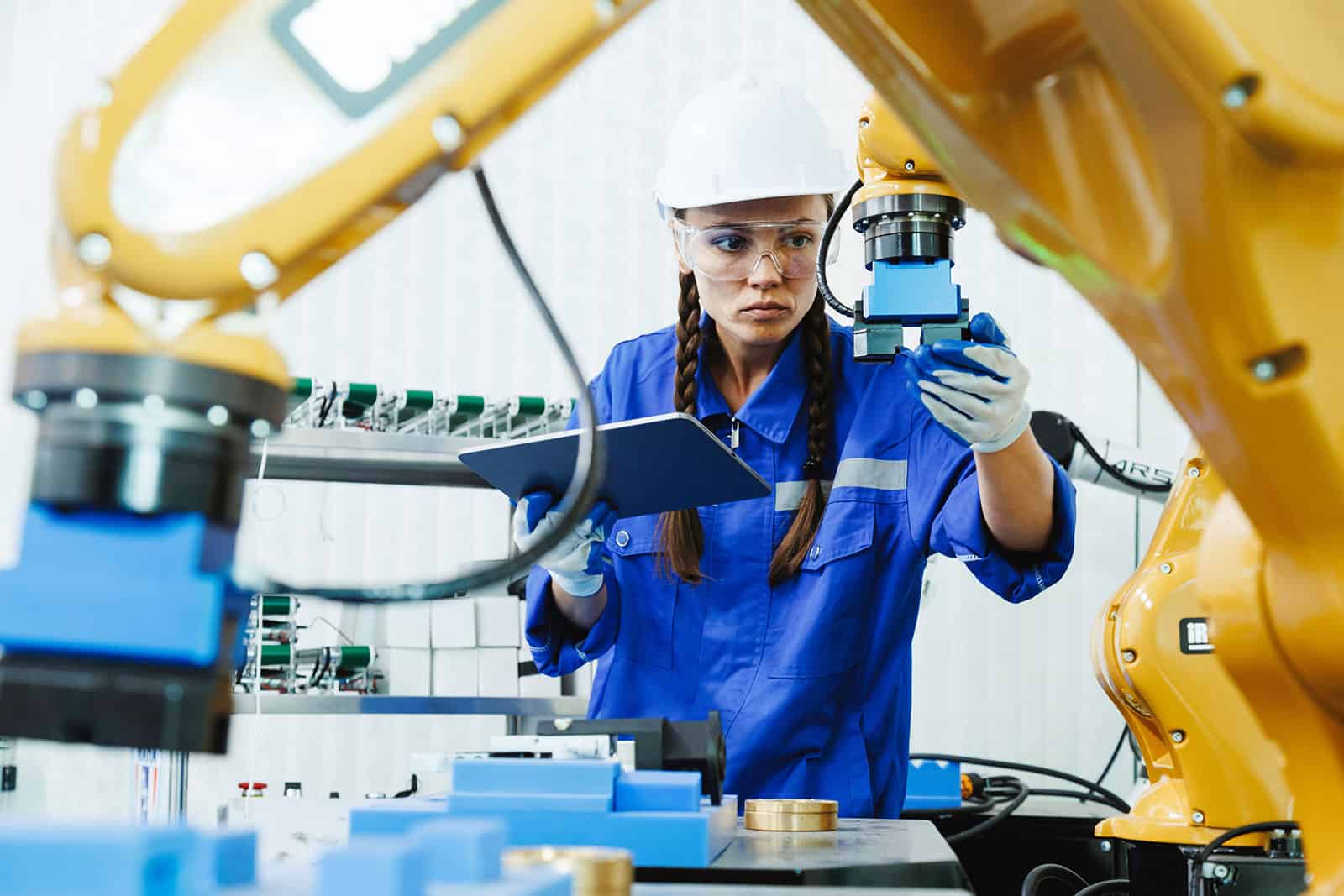 Female engineer in safety gear working with robotic machinery in an engineering environment.