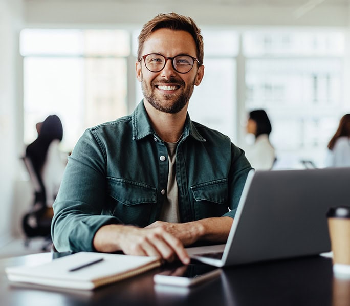 Man smiling at laptop during display screen equipment assessment in office.