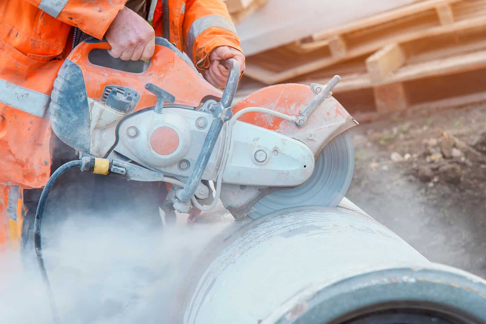Worker cutting concrete pipe with a power saw at construction site.