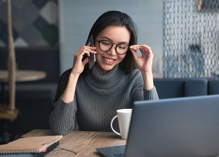 Woman smiling on phone during online meeting, working on laptop.