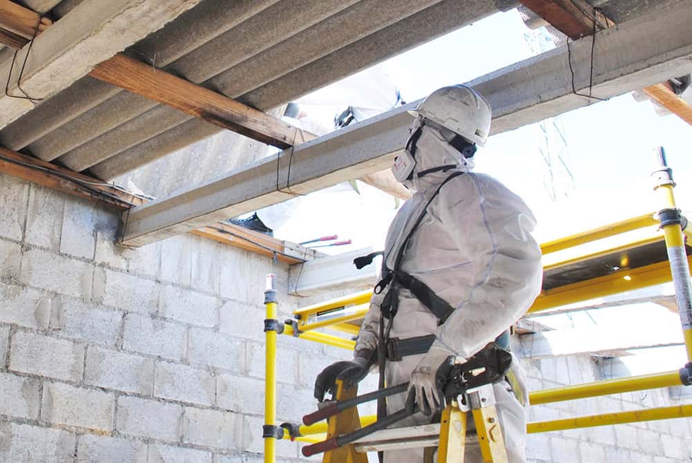 Worker in full PPE conducting health surveillance inspection at construction site.