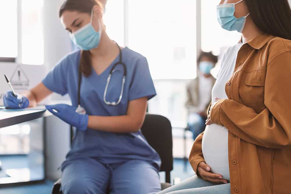 Nursing student and pregnant woman wearing masks in a healthcare setting.