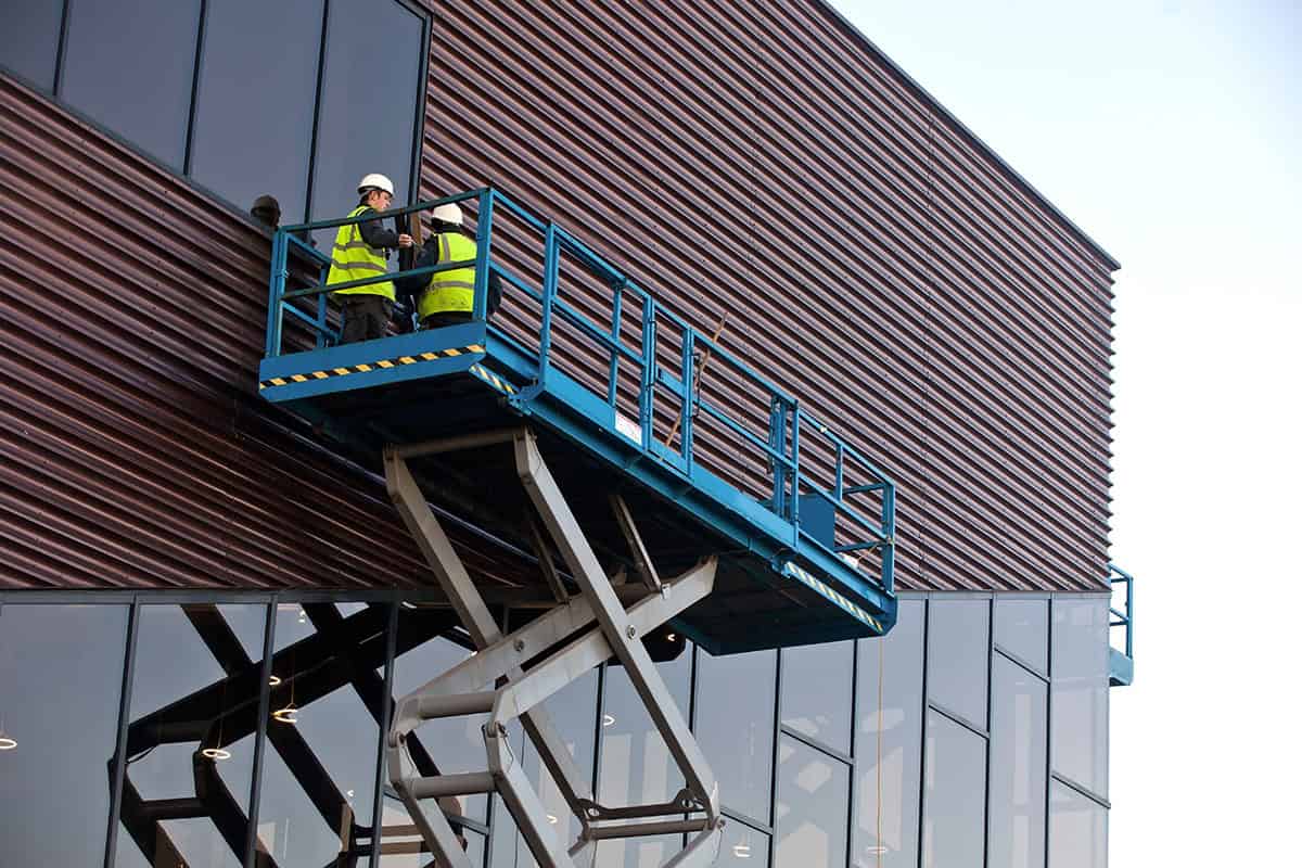 Workers on elevated platform inspecting building exterior for utility safety.