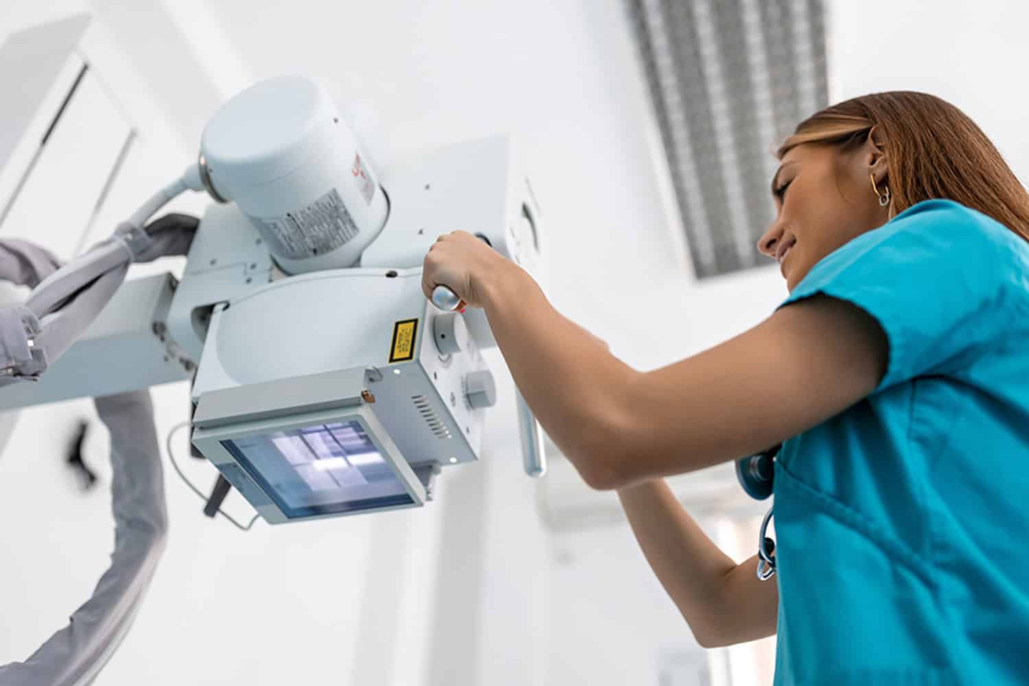 Medical professional adjusting ionising radiation equipment in a clinical setting.