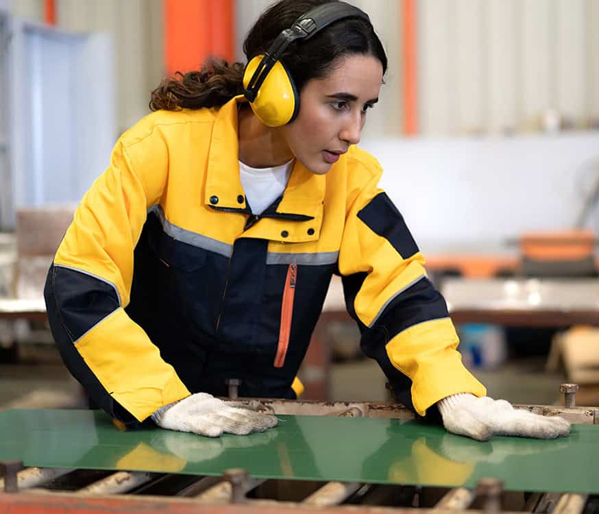 Female utility worker inspecting equipment with safety gear in industrial setting.