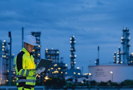 Industrial worker in safety gear reviewing plans at an industrial site.