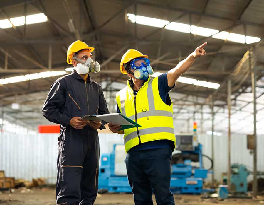 Two workers in protective gear conducting air quality testing with breathing apparatus in industrial.
