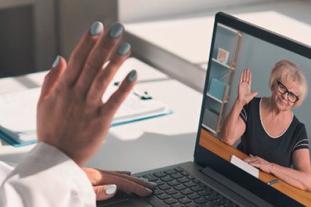 Woman on video call with elderly lady using YODHA app on laptop.