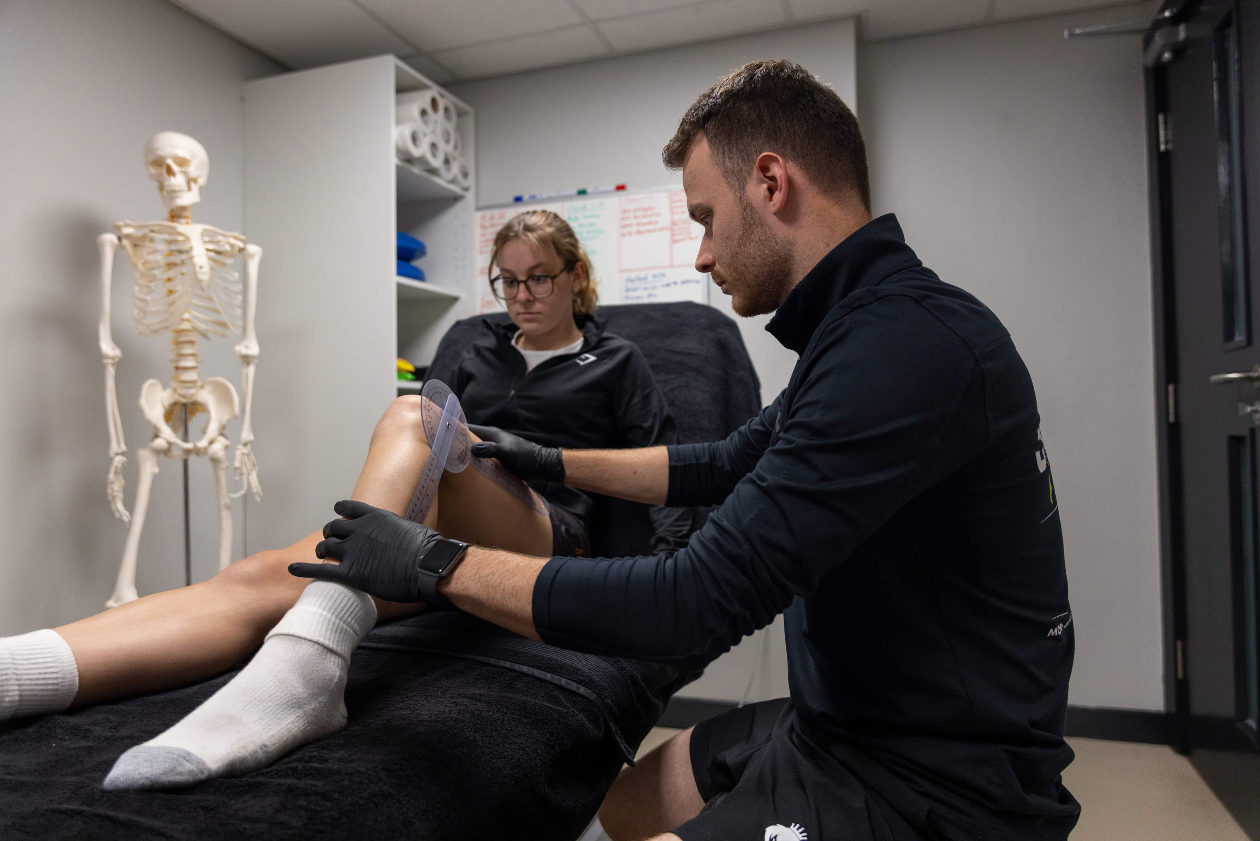 Physiotherapist examining an athlete's leg injury in a clinical setting.