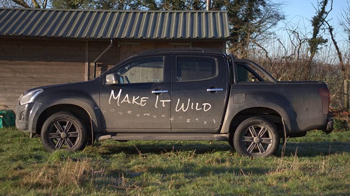 Black pickup truck with "Make It Wild" graffiti parked outdoors.
