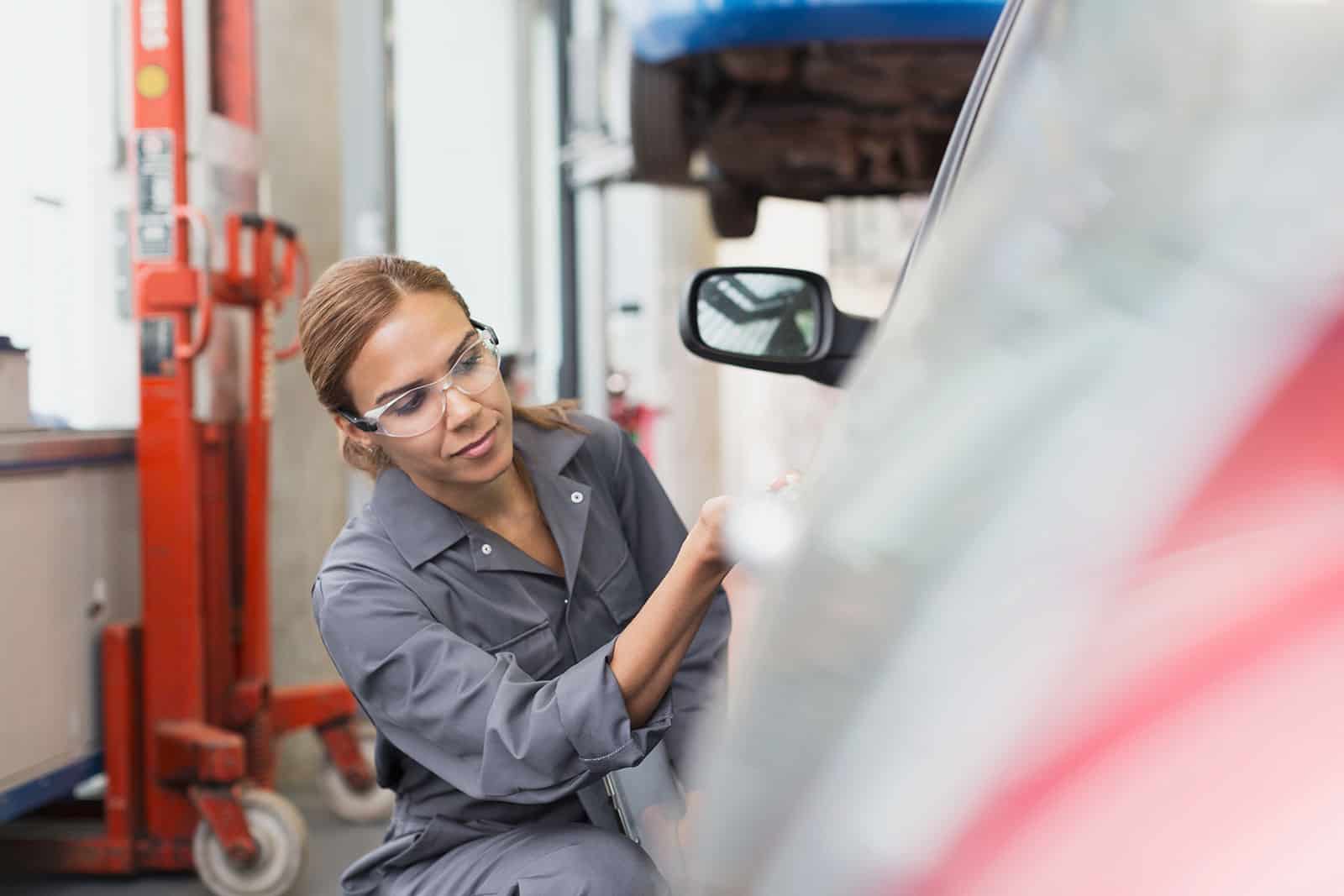 Female technician inspecting vehicle in workshop for occupational health safety.