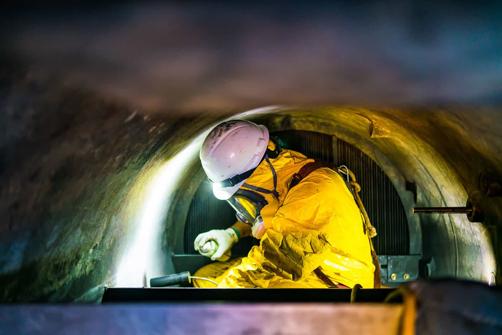 Tunnel worker inspecting a pipe in confined space for occupational health safety.