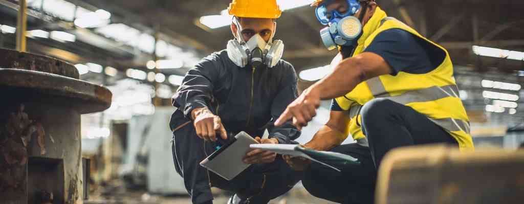 Industrial workers conducting face fit testing with safety gear in factory setting.