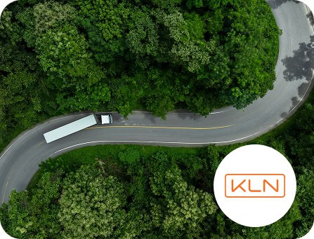 Aerial view of a winding road through a green forest, featuring a white bus and the KLN logo.